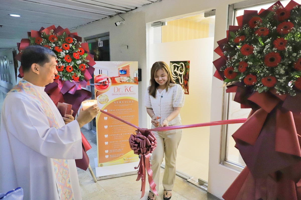 Dr. KC cutting a ribbon at the clinic entrance as a priest blesses the new clinic