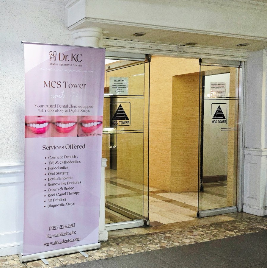 Dr. KC Dental Aesthetic Center banner standing beside the glass doors of the MCS Tower entrance
